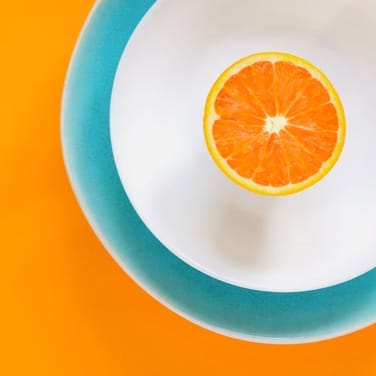 An orange sliced in half, in a plate on an orange colored surface