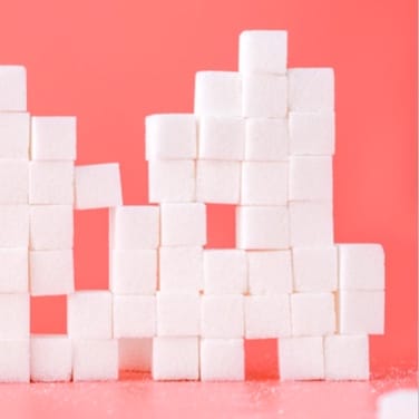 Sugar cubes stacked on top of each other in front of a pink background on a slightly lighter shade pink surface